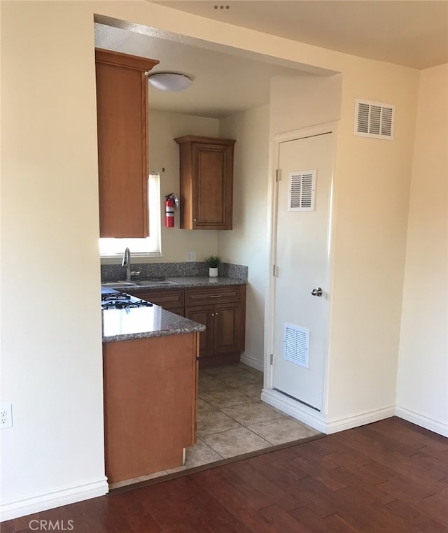 kitchen with light wood-type flooring, dark stone countertops, and sink