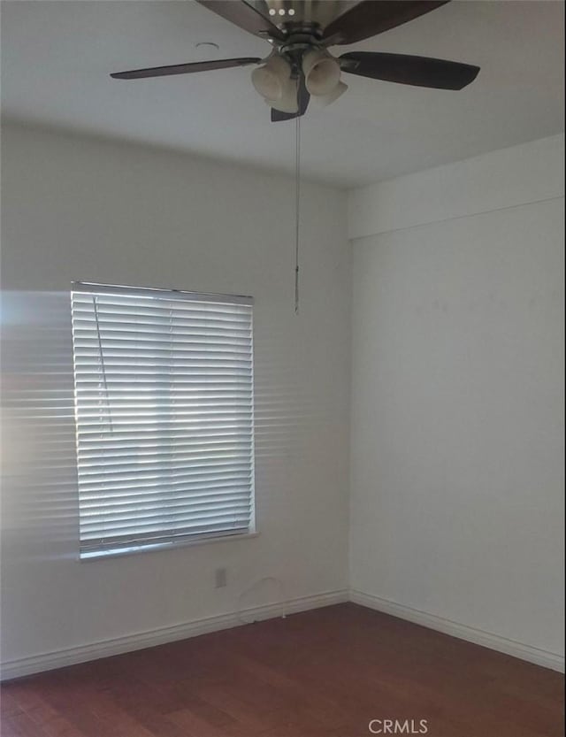 spare room featuring dark wood-type flooring, a ceiling fan, and baseboards