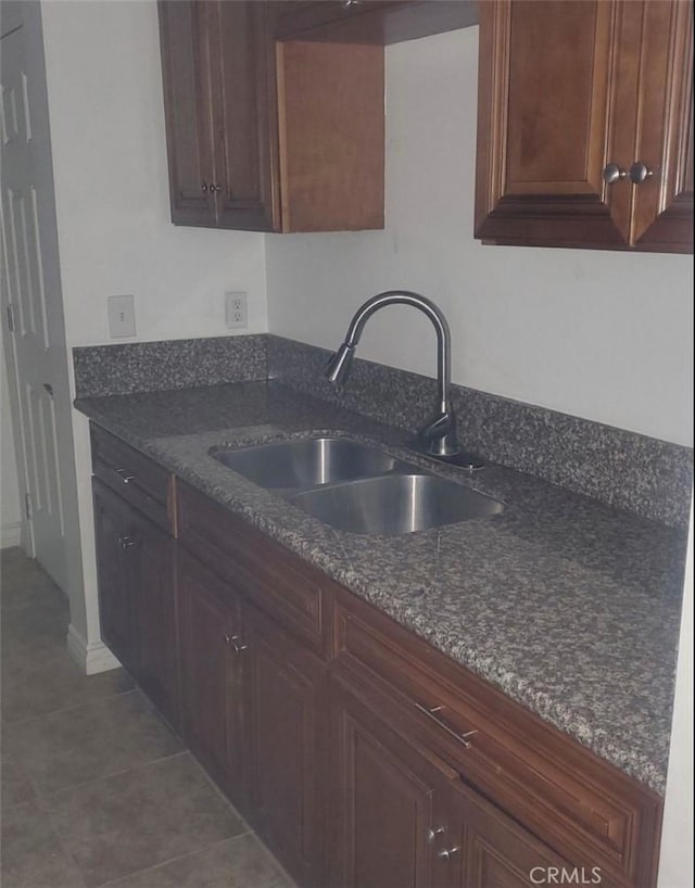 kitchen with dark tile patterned flooring, a sink, and dark stone countertops