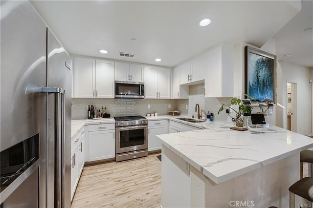 kitchen featuring stainless steel appliances, sink, kitchen peninsula, and white cabinetry