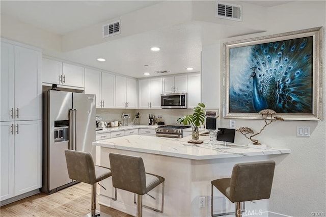 kitchen featuring light hardwood / wood-style flooring, white cabinets, appliances with stainless steel finishes, and a breakfast bar area