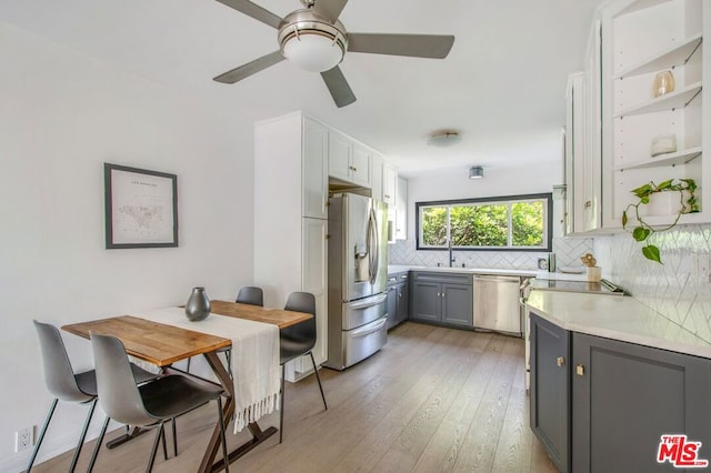 kitchen with light hardwood / wood-style flooring, ceiling fan, gray cabinets, appliances with stainless steel finishes, and tasteful backsplash