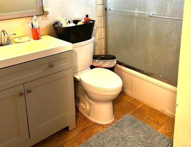 full bathroom featuring vanity, bath / shower combo with glass door, hardwood / wood-style flooring, and toilet