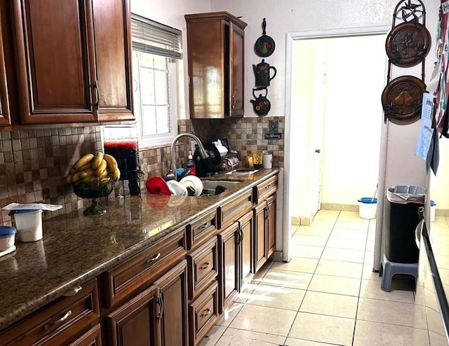 kitchen featuring light tile patterned floors, dark stone counters, sink, and decorative backsplash