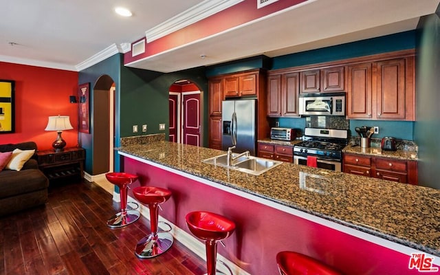 kitchen with appliances with stainless steel finishes, dark stone countertops, a breakfast bar, dark hardwood / wood-style flooring, and ornamental molding