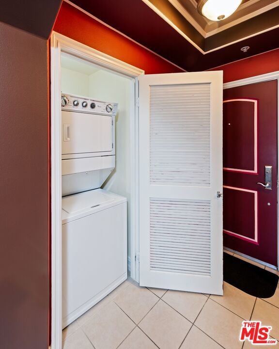 laundry area with stacked washing maching and dryer and tile patterned flooring