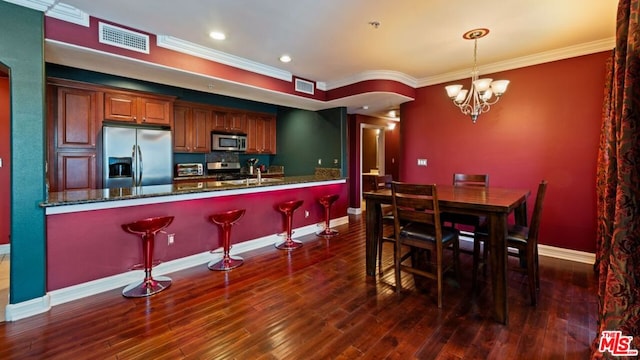 kitchen with appliances with stainless steel finishes, hanging light fixtures, ornamental molding, and dark wood-type flooring