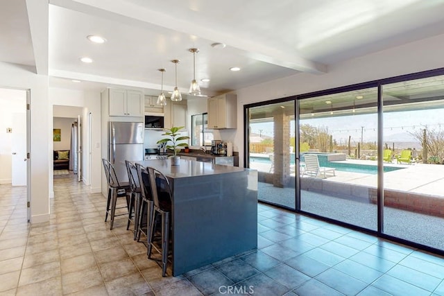 kitchen featuring stainless steel fridge, gray cabinetry, light tile patterned flooring, beam ceiling, and decorative light fixtures