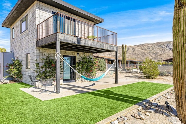 rear view of property featuring a yard, a balcony, a mountain view, and a patio area