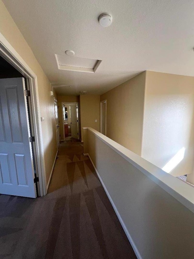 hallway featuring dark carpet and a textured ceiling