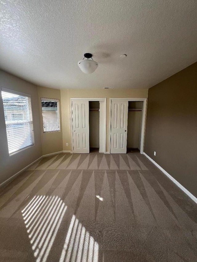 unfurnished bedroom featuring multiple closets, carpet, and a textured ceiling