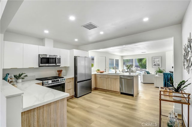 kitchen featuring light brown cabinets, white cabinets, light hardwood / wood-style floors, kitchen peninsula, and appliances with stainless steel finishes