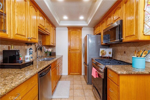 kitchen with decorative backsplash, appliances with stainless steel finishes, light stone countertops, a raised ceiling, and sink