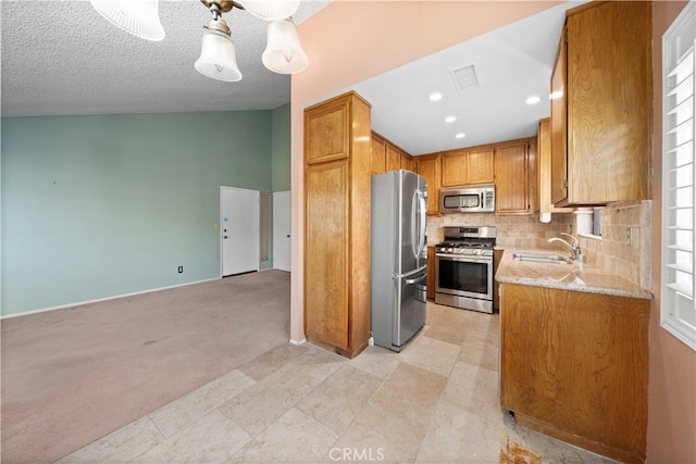 kitchen featuring sink, a textured ceiling, stainless steel appliances, light carpet, and vaulted ceiling