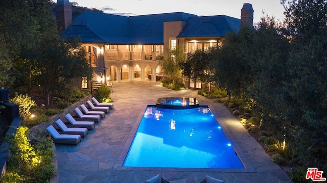 pool at dusk featuring an in ground hot tub and a patio