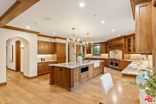 kitchen with pendant lighting, light wood-type flooring, stainless steel appliances, and a center island with sink