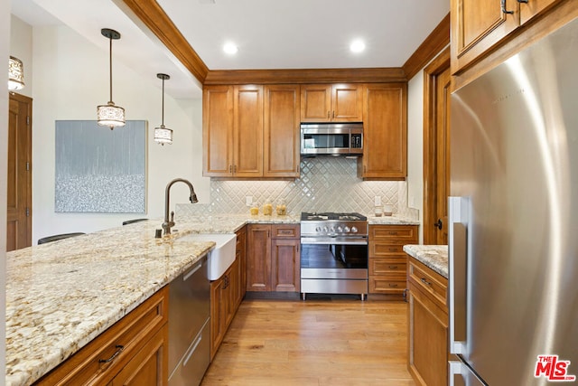 kitchen featuring appliances with stainless steel finishes, light stone counters, sink, light hardwood / wood-style flooring, and hanging light fixtures