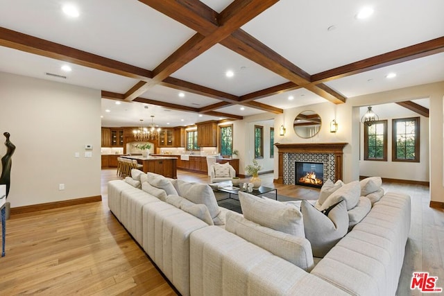 living room with a tile fireplace, coffered ceiling, light hardwood / wood-style flooring, beam ceiling, and a chandelier