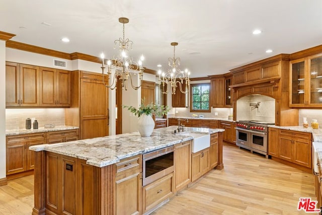 kitchen featuring sink, stainless steel appliances, a notable chandelier, decorative light fixtures, and a center island with sink