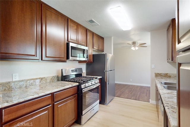 kitchen featuring ceiling fan, light hardwood / wood-style flooring, light stone counters, sink, and stainless steel appliances