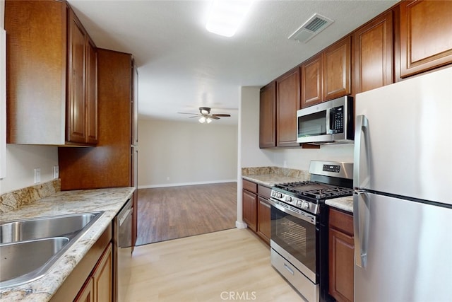 kitchen featuring ceiling fan, light stone countertops, appliances with stainless steel finishes, and light hardwood / wood-style floors