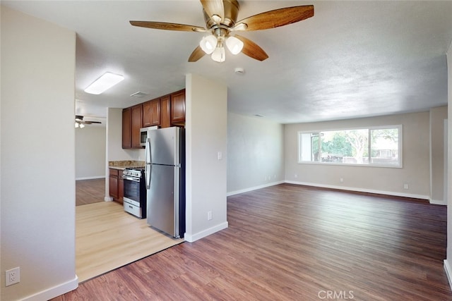 kitchen featuring light stone counters, ceiling fan, a textured ceiling, stainless steel appliances, and light wood-type flooring