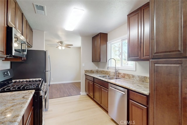 kitchen with light wood-type flooring, ceiling fan, sink, appliances with stainless steel finishes, and a textured ceiling