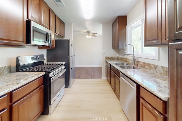 kitchen with light hardwood / wood-style floors, appliances with stainless steel finishes, sink, and light stone counters