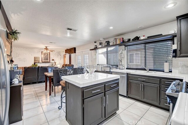 kitchen featuring tile countertops, a kitchen island, a textured ceiling, and appliances with stainless steel finishes