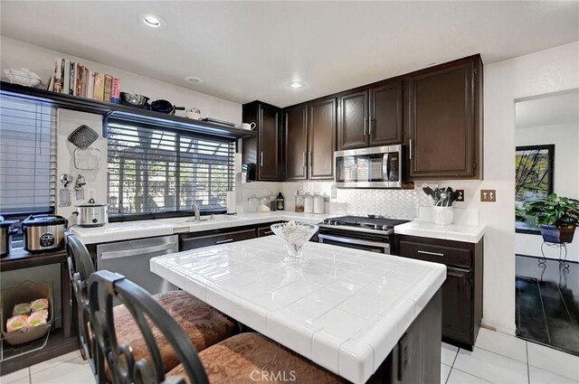 kitchen with appliances with stainless steel finishes, backsplash, sink, a kitchen island, and light tile patterned flooring