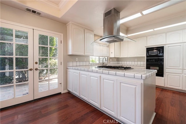 kitchen with island exhaust hood, dark hardwood / wood-style flooring, tile countertops, and black appliances