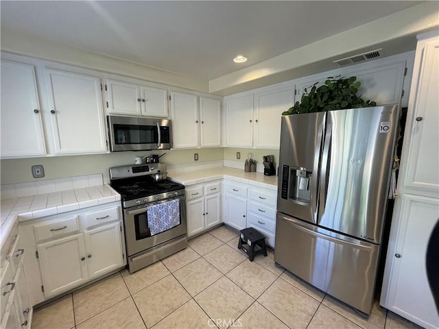 kitchen featuring tile counters, white cabinets, stainless steel appliances, and light tile patterned floors