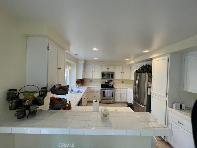 kitchen with kitchen peninsula, tile countertops, white cabinetry, and stainless steel appliances