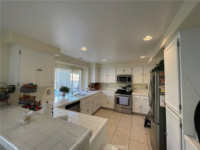 kitchen featuring kitchen peninsula, appliances with stainless steel finishes, white cabinetry, and tile counters