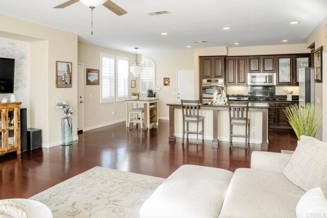 living room with ceiling fan with notable chandelier and dark wood-type flooring