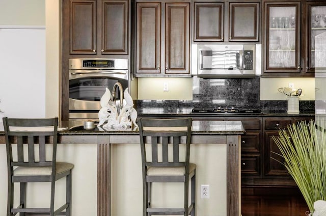 kitchen featuring dark stone counters, black gas cooktop, dark brown cabinetry, and a breakfast bar