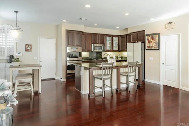 kitchen featuring hanging light fixtures, dark brown cabinets, a center island with sink, appliances with stainless steel finishes, and dark hardwood / wood-style flooring