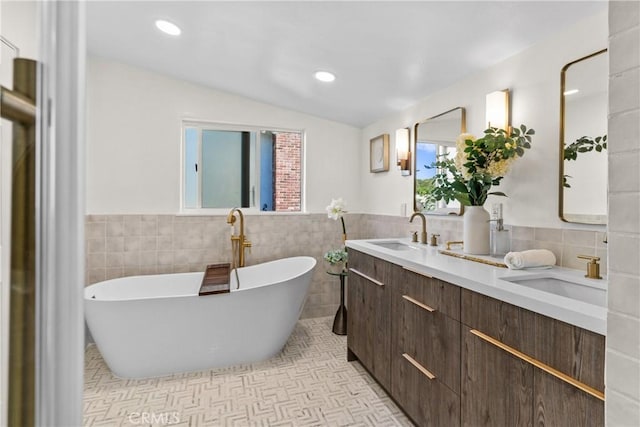 bathroom with vaulted ceiling, tile walls, a bathtub, vanity, and tile patterned floors