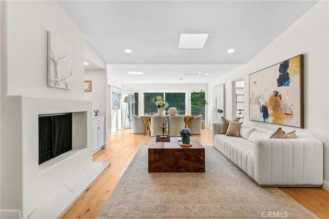 living room with a skylight, a high end fireplace, and light hardwood / wood-style floors