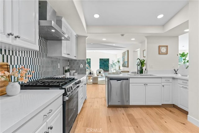 kitchen featuring wall chimney range hood, sink, stainless steel appliances, white cabinets, and light wood-type flooring