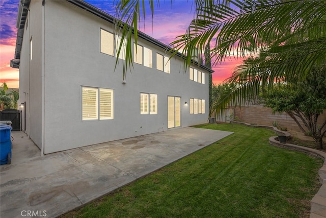 back house at dusk featuring a patio area and a yard