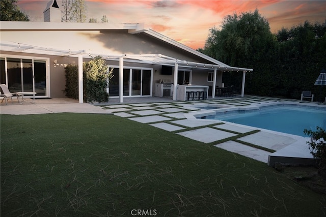 pool at dusk with a yard, a patio area, an outdoor pool, and outdoor dry bar