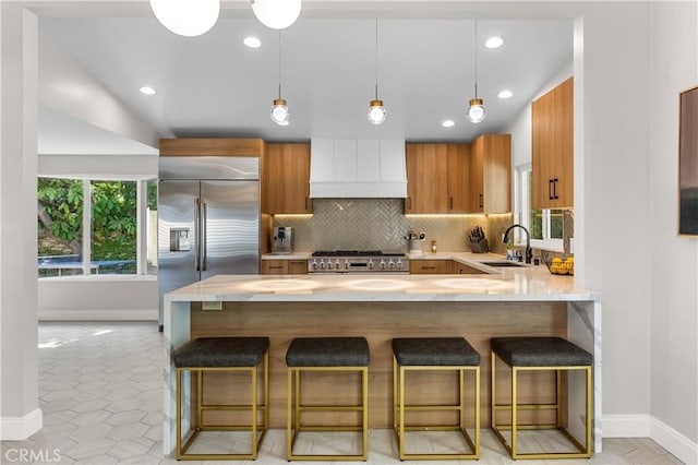 kitchen featuring backsplash, built in refrigerator, custom range hood, a peninsula, and a sink