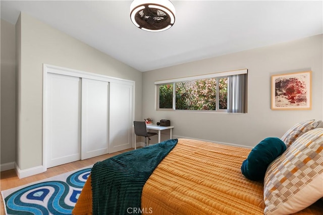 bedroom featuring light wood-type flooring, baseboards, a closet, and vaulted ceiling