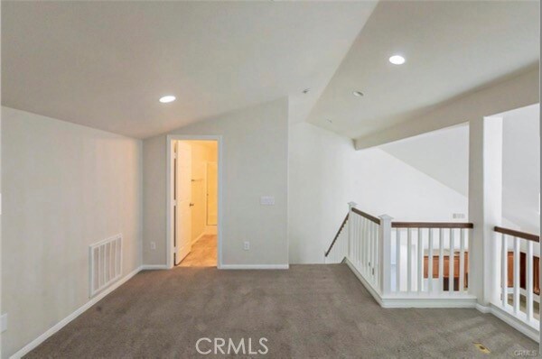 spare room featuring dark colored carpet and vaulted ceiling