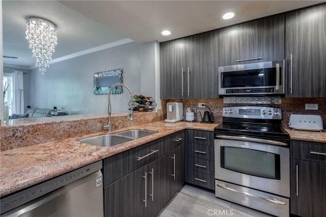 kitchen with light stone countertops, appliances with stainless steel finishes, ornamental molding, sink, and a chandelier