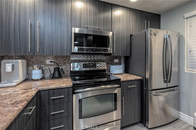 kitchen featuring light stone counters, light wood-type flooring, appliances with stainless steel finishes, and tasteful backsplash