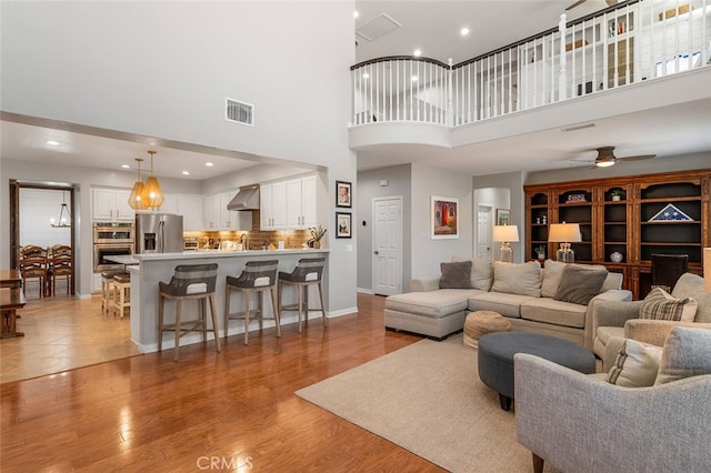 living room with ceiling fan, sink, light hardwood / wood-style flooring, and a high ceiling