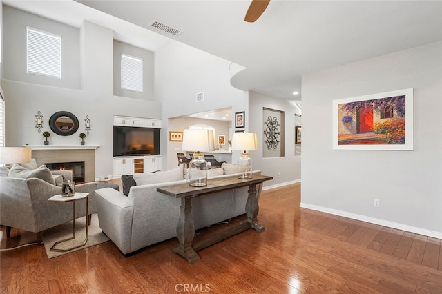 living room featuring wood-type flooring, a towering ceiling, and a tile fireplace