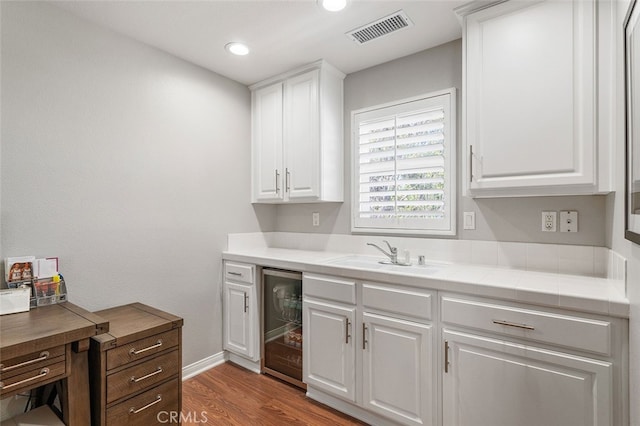 kitchen with white cabinets, beverage cooler, sink, and hardwood / wood-style flooring